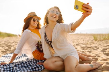 Sahilde selfie çeken iki güzel kadın. Pozitif modeller eğleniyor. Seyahat, blog, hafta sonu, rahatlama ve yaşam tarzı konsepti.