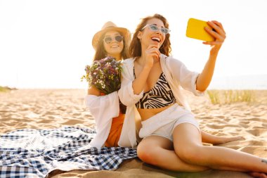 Sahilde selfie çeken iki güzel kadın. Pozitif modeller eğleniyor. Seyahat, blog, hafta sonu, rahatlama ve yaşam tarzı konsepti.