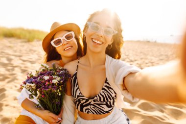Sahilde selfie çeken iki güzel kadın. Pozitif modeller eğleniyor. Seyahat, blog, hafta sonu, rahatlama ve yaşam tarzı konsepti.