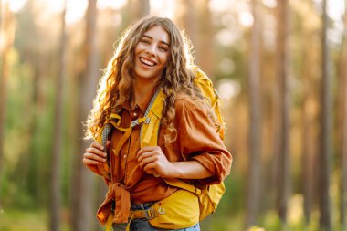Kadın turist sarı sırt çantasıyla ormanda yürüyüş yapıyor. Tarz sahibi dişi, büyük ağaçlar arasında yol arar. Etkin yaşam biçimi.