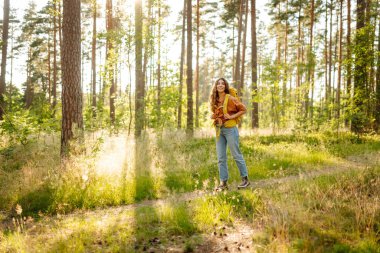 Sırt çantalı kadın turist ormandaki temiz havada dinleniyor, mutluluğu ve doğayla bağlantıyı hissediyor..