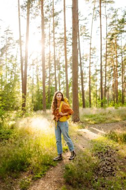 Sırt çantalı kadın turist ormandaki temiz havada dinleniyor, mutluluğu ve doğayla bağlantıyı hissediyor..