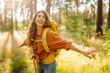 Sırt çantalı kadın turist ormandaki temiz havada dinleniyor, mutluluğu ve doğayla bağlantıyı hissediyor..