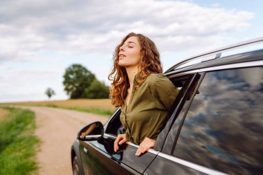 Arabayla ya da karavanla seyahat eden genç bir kadın, açık pencere kırsal alanda temiz hava alıyor. Seyahat macerası..