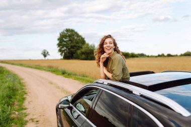 Arabayla ya da karavanla seyahat eden genç bir kadın, açık pencere kırsal alanda temiz hava alıyor. Seyahat macerası..