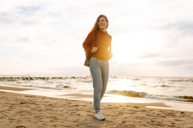 Soğuk havada kumsalda sırt çantalı güzel bir kadının portresi. Denize yakın bir sonbahar. Sakinlik ve sükunet. Seyahat, turizm konsepti.