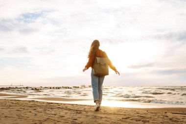 Soğuk havada kumsalda sırt çantalı güzel bir kadının portresi. Denize yakın bir sonbahar. Sakinlik ve sükunet. Seyahat, turizm konsepti.