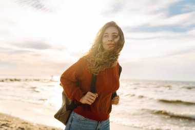 Soğuk havada kumsalda sırt çantalı güzel bir kadının portresi. Denize yakın bir sonbahar. Sakinlik ve sükunet. Seyahat, turizm konsepti.