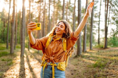 Güneşli bir günde ormanlık alanda ağaçların yanında selfie çeken güzel bir kadın. Seyahat blogu. Macera, tatil.