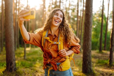 Güneşli bir günde ormanlık alanda ağaçların yanında selfie çeken güzel bir kadın. Seyahat blogu. Macera, tatil.