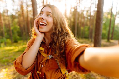 Güneşli bir günde ormanlık alanda ağaçların yanında selfie çeken güzel bir kadın. Seyahat blogu. Macera, tatil.