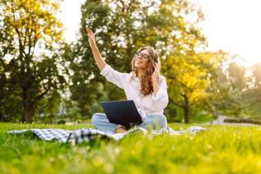 Genç bayan kulaklıklar oturup müzik dinlerler cep telefonu kullanırlar. Dinle, müzik parkta yeşil çimlerin üzerinde çalışıyor, çalışıyor. Eğitim, iş, blog veya serbest çalışma kavramı.