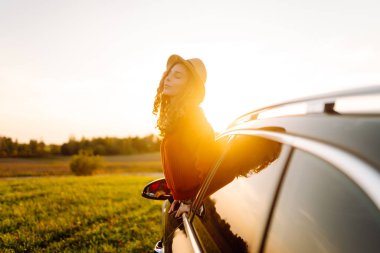 Mutlu kadın araba penceresinden gün batımını seyretmeyi sever. Yaşam tarzı, seyahat, turizm, doğa, aktif yaşam.