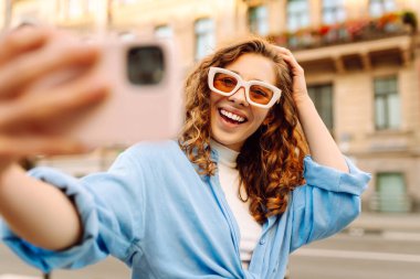 Güzel kadın gezgin telefon kullanıyor, selfie çekiyor, eski şehir caddesinde yürüyor. Blogculuk, teknoloji, yaşam tarzı, seyahat, turizm, aktif yaşam