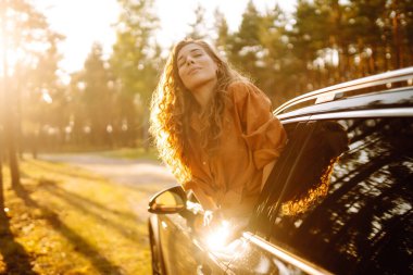Gün batımında arabayla seyahat eden mutlu, rahat bir kadın. Yolculuklar. Doğa manzarası.