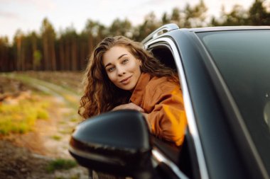 Gün batımında arabayla seyahat eden mutlu, rahat bir kadın. Yolculuklar. Doğa manzarası.