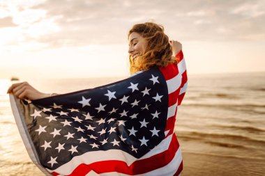 Okyanusta yürüyen Amerikan bayrağı taşıyan genç bir kadın. 4 Temmuz. Amerika Bağımsızlık Günü konsepti.