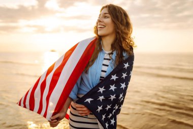 Okyanusta yürüyen Amerikan bayrağı taşıyan genç bir kadın. 4 Temmuz. Amerika Bağımsızlık Günü konsepti.