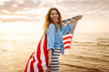Okyanusta yürüyen Amerikan bayrağı taşıyan genç bir kadın. 4 Temmuz. Amerika Bağımsızlık Günü konsepti.