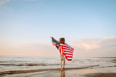 Okyanusta yürüyen Amerikan bayrağı taşıyan genç bir kadın. 4 Temmuz. Amerika Bağımsızlık Günü konsepti.