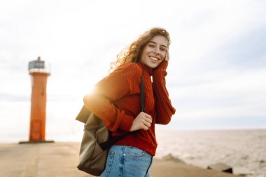 Deniz aşırı deniz fenerine bakan genç bir kadın. Seyahat, hafta sonu, rahatlama ve yaşam tarzı konsepti.