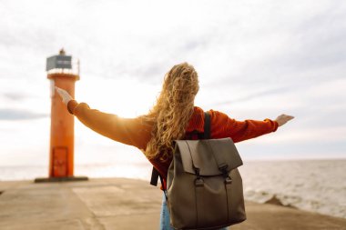 Deniz aşırı deniz fenerine bakan genç bir kadın. Seyahat, hafta sonu, rahatlama ve yaşam tarzı konsepti.