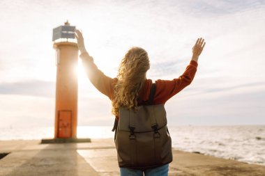 Deniz aşırı deniz fenerine bakan genç bir kadın. Seyahat, hafta sonu, rahatlama ve yaşam tarzı konsepti.
