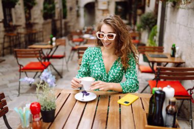 Genç ve şık bir kadın kahvesini kahve içerken kafedeki terasta oturuyor. Yiyecek ve içecek. İnsanlar, moda, yaşam tarzı, seyahat ve tatil kavramı