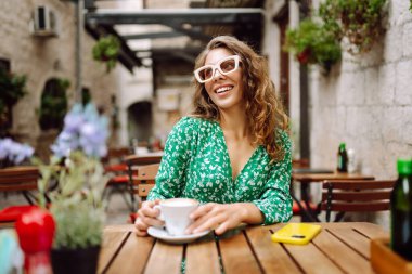 Genç ve şık bir kadın kahvesini kahve içerken kafedeki terasta oturuyor. Yiyecek ve içecek. İnsanlar, moda, yaşam tarzı, seyahat ve tatil kavramı