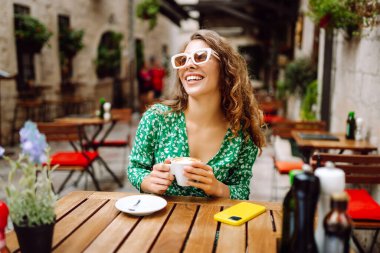 Genç ve şık bir kadın kahvesini kahve içerken kafedeki terasta oturuyor. Yiyecek ve içecek. İnsanlar, moda, yaşam tarzı, seyahat ve tatil kavramı