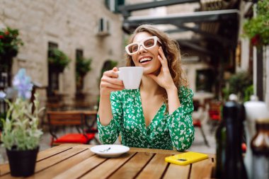 Genç ve şık bir kadın kahvesini kahve içerken kafedeki terasta oturuyor. Yiyecek ve içecek. İnsanlar, moda, yaşam tarzı, seyahat ve tatil kavramı