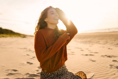 Soğuk havada, boş deniz kıyısında tek başına yürüyen güzel bir kadının portresi. Gün batımı. Yalnız kadın özgürlüğü kavramı. Seyahat, turizm konsepti.