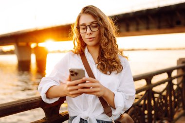 Kafkasyalı genç bir kadın setin üzerinde yürürken akıllı telefonunu kullanıyor. Meslek, blog, teknoloji kavramı, hafta sonu.