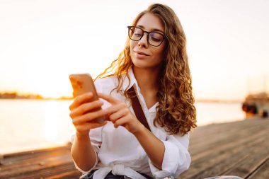 Kafkasyalı genç bir kadın setin üzerinde yürürken akıllı telefonunu kullanıyor. Meslek, blog, teknoloji kavramı, hafta sonu.