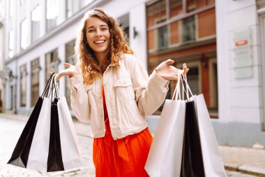 Alışveriş yaptıktan sonra şehirde dolaşan alışveriş çantalı bir kadın. Bahar alışverişi. Ticaret ve indirimler.