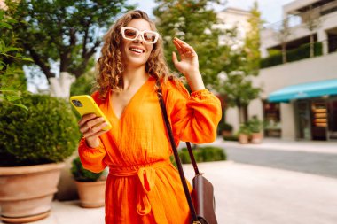 Dışarıda yürürken cep telefonunda gülen ve mesaj atan genç bir kadın. Yaşam tarzı, seyahat, turizm, teknoloji, blog yazma, iletişim kavramı.