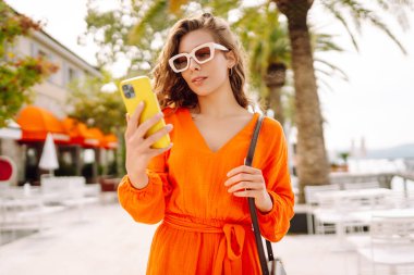 Dışarıda yürürken cep telefonunda gülen ve mesaj atan genç bir kadın. Yaşam tarzı, seyahat, turizm, teknoloji, blog yazma, iletişim kavramı.