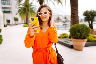 Dışarıda yürürken cep telefonunda gülen ve mesaj atan genç bir kadın. Yaşam tarzı, seyahat, turizm, teknoloji, blog yazma, iletişim kavramı.