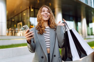 Alışveriş yaparken akıllı telefon kullanan mutlu bir kadın. Kara Cuma, indirim ve satış. Tatil için kıyafet almak..