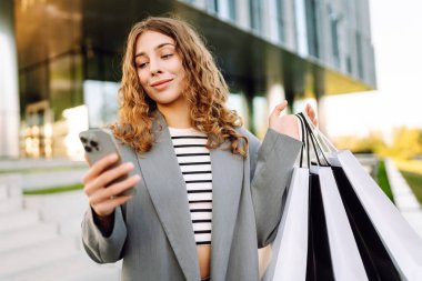 Alışveriş yaparken akıllı telefon kullanan mutlu bir kadın. Kara Cuma, indirim ve satış. Tatil için kıyafet almak..