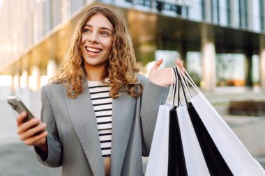 Alışveriş yaparken akıllı telefon kullanan mutlu bir kadın. Kara Cuma, indirim ve satış. Tatil için kıyafet almak..