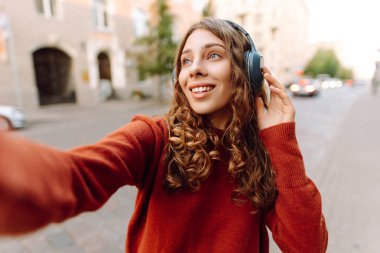 Şehirdeki bir kadın telefonla selfie çekiyor ve müzik dinliyor. Seyahat, turizm, teknoloji, blog konsepti.