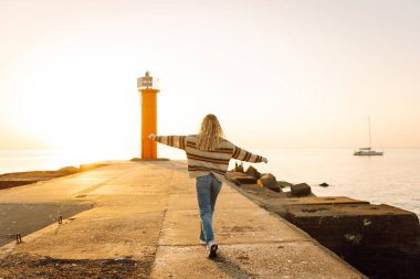 Deniz fenerinin yanındaki turist kadın. Arka planda bahar günbatımı. Seyahat, hafta sonu, rahatlama ve yaşam tarzı konsepti.