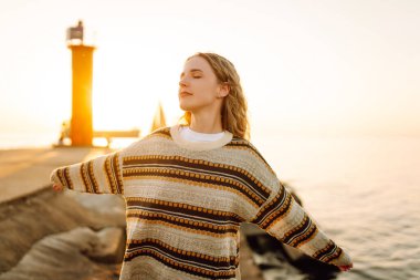 Deniz fenerinin yanındaki turist kadın. Arka planda bahar günbatımı. Seyahat, hafta sonu, rahatlama ve yaşam tarzı konsepti.