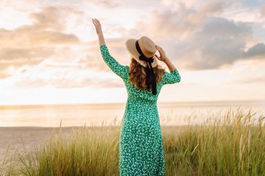 Uzun sahil çimlerinde doğanın tadını çıkaran mutlu bir kadın. Açık havada. Kıyı şeridinde moda tarzı.