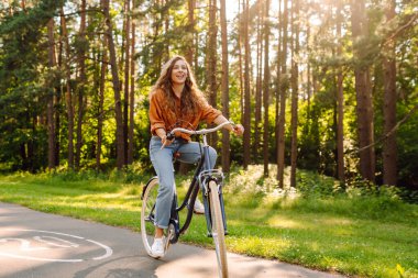 Yeşil şehir parkında kaldırımda bisiklet süren mutlu kadın. Etkin yaşam tarzı kavramı.