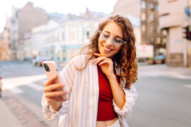 Şehir caddesinde telefon kullanan güzel bir genç kadının portresi. İletişim, sosyal ağlar, blog yazma, online alışveriş kavramı.