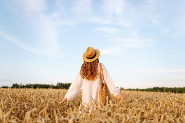 Altın buğday tarlasında özgür hisseden şık bir yaz elbisesi içinde moda bir kadın. Moda, cazibe, yaşam tarzı konsepti