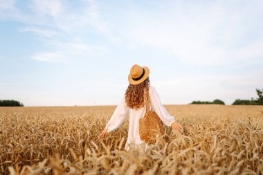 Altın buğday tarlasında özgür hisseden şık bir yaz elbisesi içinde moda bir kadın. Moda, cazibe, yaşam tarzı konsepti