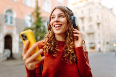 Genç, neşeli, güzel bir kadın dans ediyor ve kulaklıkla en sevdiği müziği dinliyor. Seyahat, turizm, teknoloji, blog konsepti. Kasaba yaşam tarzları.